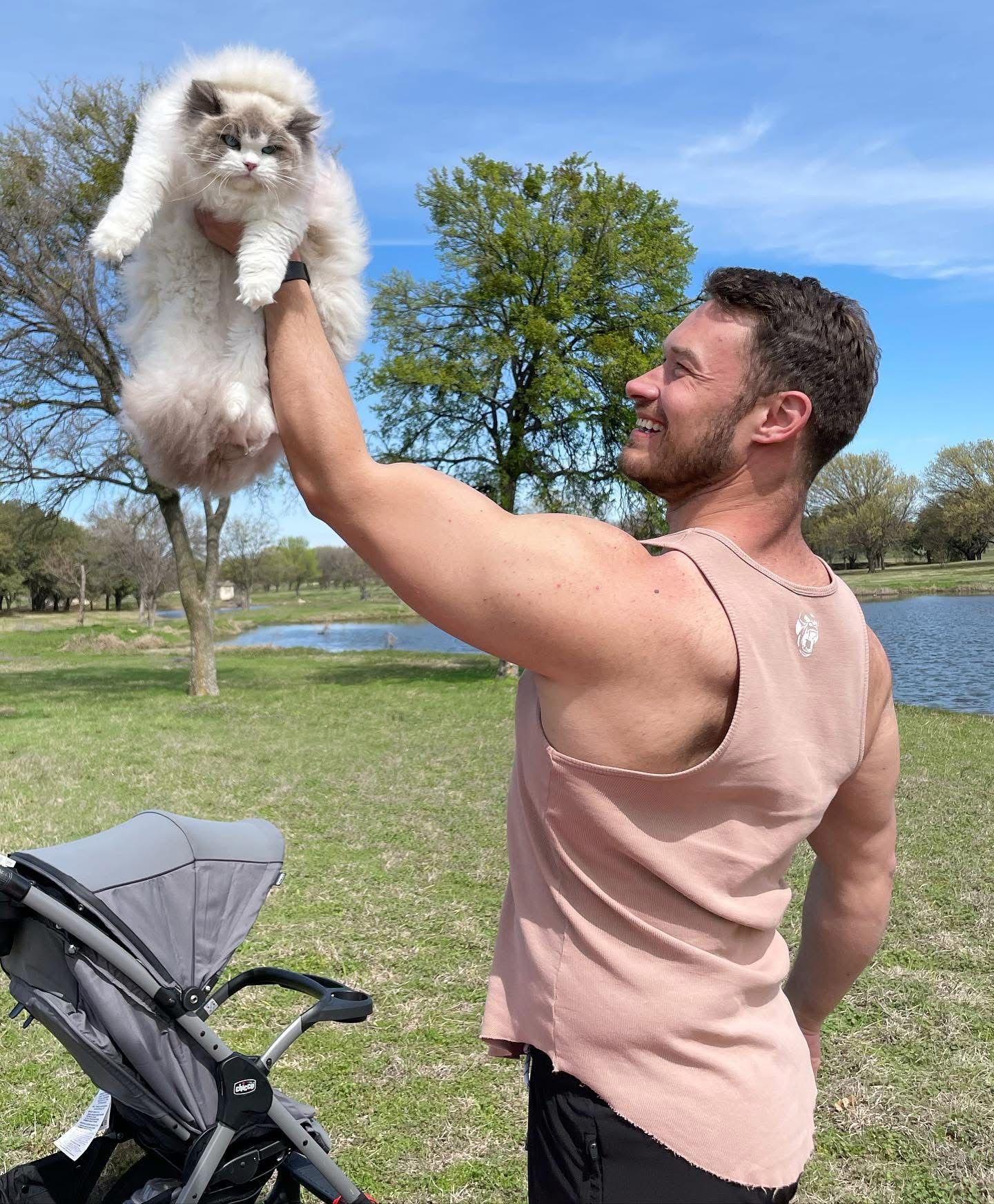 A smiling man in a park lifting a large fluffy blue bicolour Ragdoll cat towards the sky